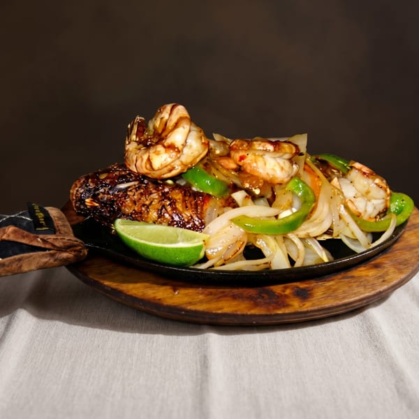 Sizzling shrimp and fish fajitas with onions, green peppers, and lime on a wooden platter.